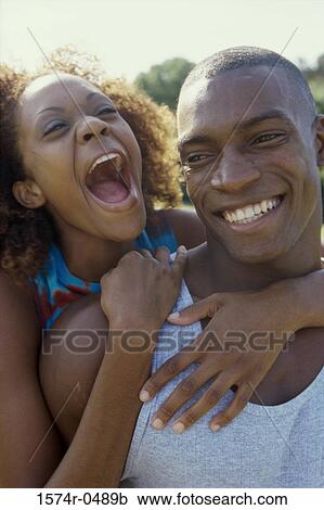 Stock Image - Young woman standing behind a young man with her arms around him. Fotosearch