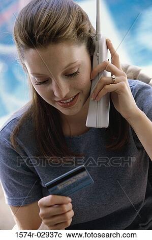 Stock Image - Young woman using a cordless phone holding a credit card. Fotosearch