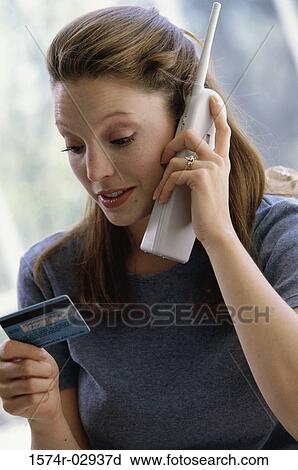 Stock Image - Young woman using a cordless phone holding a credit card. Fotosearch