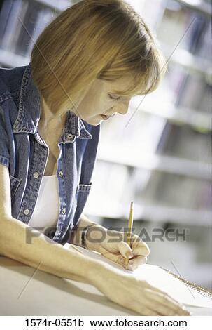 Young woman writing in a book at the library View Large Photo Image Stock Image - Young woman writing in a book at the library. Fotosearch