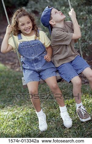 Stock Image - Boy and girl swinging on a rope swing. Fotosearch