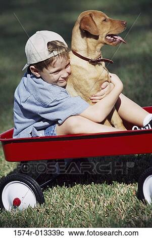 Stock Image - Boy sitting in a toy wagon holding his dog. Fotosearch