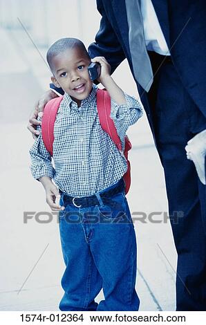 Picture - Boy talking on a mobile phone with his father standing beside him. Fotosearch