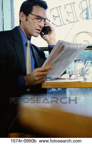 Stock Image - Businessman holding a newspaper talking on a mobile phone. Fotosearch