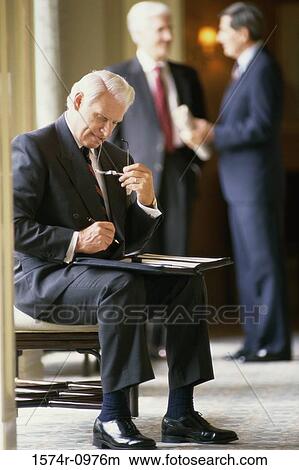 Businessman writing in a file with two businessmen standing behind him View Large Photo Image Picture - Businessman writing in a file with two businessmen standing behind him. Fotosearch