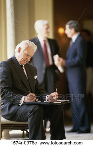 Businessman writing in a file with two businessmen standing behind him View Large Photo Image Stock Image - Businessman writing in a file with two businessmen standing behind him. Fotosearch