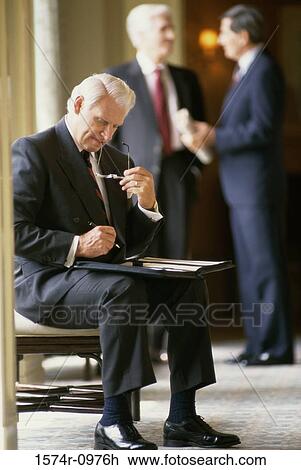 Stock Image - Businessman writing in a file with two businessmen standing behind him. Fotosearch