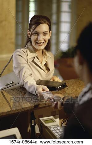 Stock Image - Businesswoman handing a credit card to a hotel clerk. Fotosearch