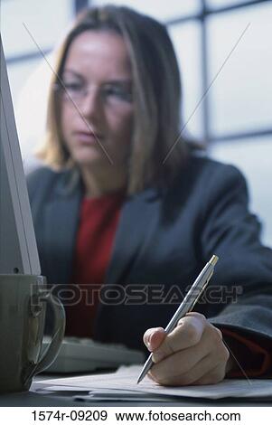 Stock Photo - Businesswoman holding a pen while looking at a computer monitor. Fotosearch