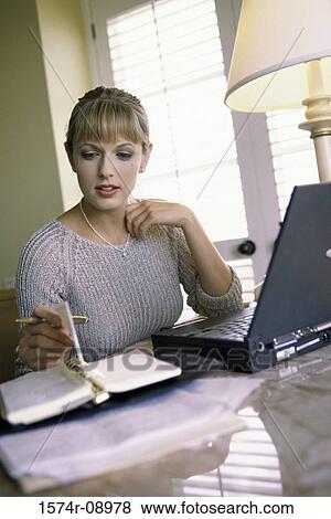 Stock Photo - Businesswoman sitting in front of a laptop reading a diary. Fotosearch