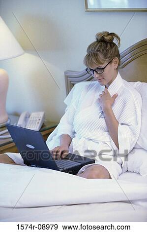Businesswoman sitting on a bed and working on a laptop View Large Photo Image Stock Photo - Businesswoman sitting on a bed and working on a laptop. Fotosearch