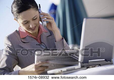 Businesswoman talking on a mobile phone while reading a newspaper View Large Photo Image Stock Image - Businesswoman talking on a mobile phone while reading a newspaper. Fotosearch