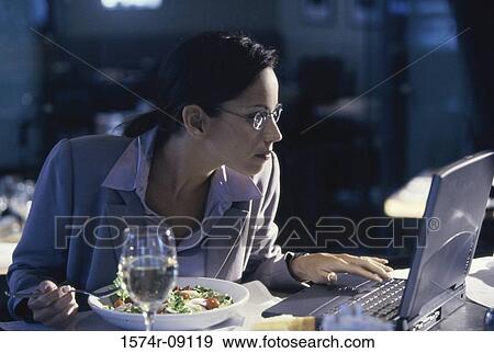 Businesswoman working on a laptop while eating a bowl of salad View Large Photo Image Stock Photo - Businesswoman working on a laptop while eating a bowl of salad. Fotosearch