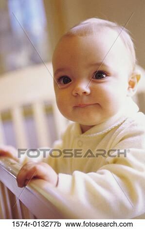 Stock Image - Close-up of a baby boy holding the railing of his crib. Fotosearch
