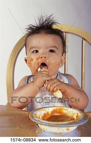 Picture - Close-up of a baby boy sitting in a high chair holding a spoon. Fotosearch