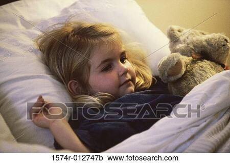 Stock Image - Close-up of a girl lying on the bed with her teddy bear. Fotosearch