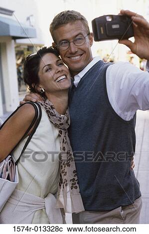 Close-up of a mid adult couple taking a photograph of themselves in a market View Large Photo Image Stock Image - Close-up of a mid adult couple taking a photograph of themselves in a market. Fotosearch