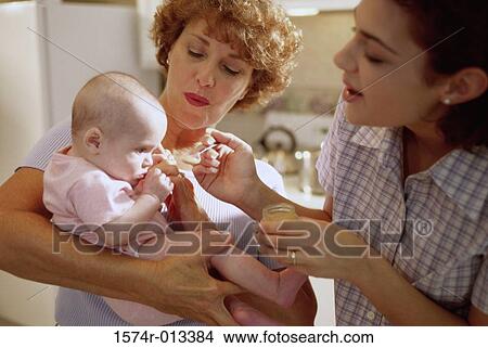 Picture - Close-up of a mother feeding her baby being held by her grandmother. Fotosearch