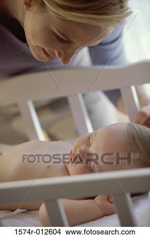 Picture - Close-up of a mother looking at her son sleeping in a crib. Fotosearch