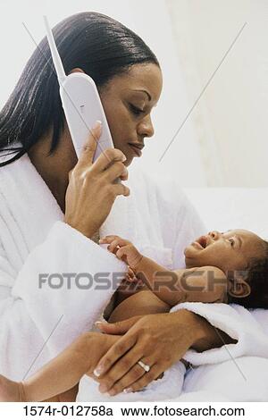 Stock Image - Close-up of a mother using a phone while holding her son. Fotosearch