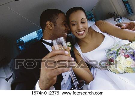 Stock Photography - Close-up of a newlywed couple sitting in a limousine toasting with champagne. Fotosearch
