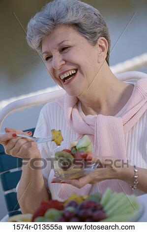 Stock Image - Close-up of a senior woman holding a bowl of fruit salad. Fotosearch