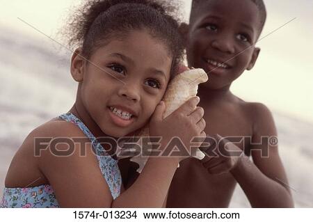 Close-up of a sister listening in a conch shell with her brother beside her View Large Photo Image Picture - Close-up of a sister listening in a conch shell with her brother beside her. Fotosearch