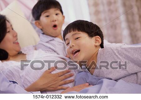 Stock Image - Close-up of a son with his head against his pregnant mother's abdomen. Fotosearch