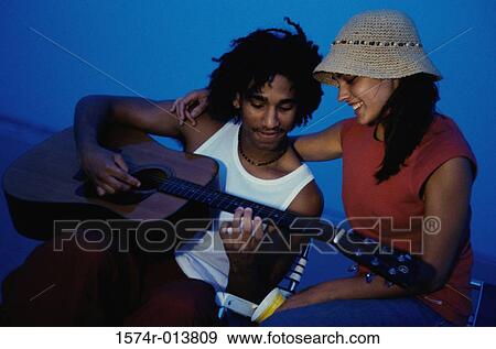 Close-up of a teenage boy playing a guitar with a teenage girl sitting beside him View Large Photo Image Stock Photo - Close-up of a teenage boy playing a guitar with a teenage girl sitting beside him. Fotosearch