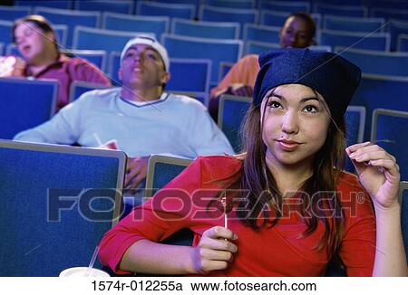 Stock Image - Close-up of a teenage girl sitting in a movie theater with a lollipop. Fotosearch