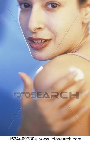Stock Image - Close-up of a woman applying moisturizer on her shoulder. Fotosearch
