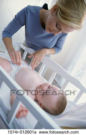 Close-up of a woman checking her son's diaper in a crib View Large Photo Image Stock Image - Close-up of a woman checking her son's diaper in a crib. Fotosearch