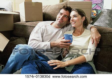 Stock Image - Close-up of a young couple holding a cup of coffee sitting on the floor. Fotosearch