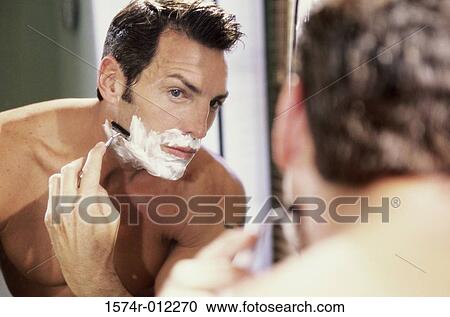 Stock Image - Close-up of a young man shaving in the bathroom. Fotosearch