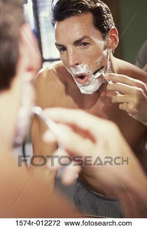Stock Image - Close-up of a young man shaving in the bathroom. Fotosearch