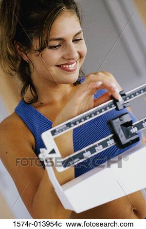 Stock Image - Close-up of a young woman adjusting a weight scale. Fotosearch