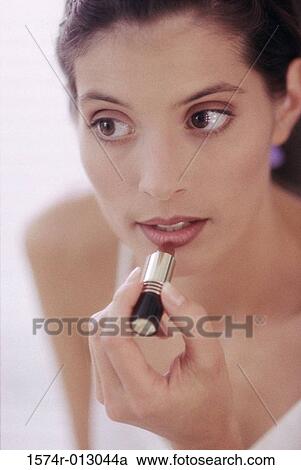 Stock Image - Close-up of a young woman applying lipstick. Fotosearch