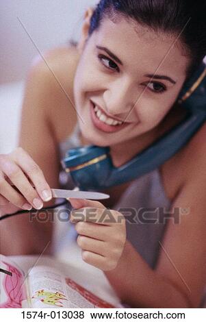 Close-up of a young woman filing her fingernails while talking on the telephone View Large Photo Image Stock Photo - Close-up of a young woman filing her fingernails while talking on the telephone. Fotosearch