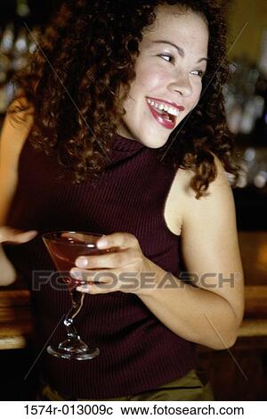 Stock Image - Close-up of a young woman holding a glass of martini and smiling. Fotosearch