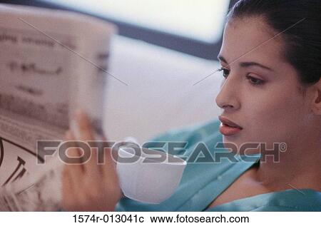Stock Image - Close-up of a young woman reading a newspaper and drinking coffee. Fotosearch