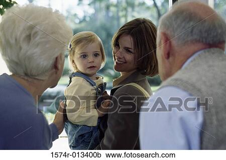 Stock Image - Close-up of grandparents greeting their daughter and granddaughter at the front door. Fotosearch