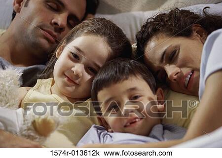 Stock Image - Close-up of parents with their two children lying on the bed. Fotosearch