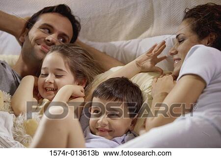 Close-up of parents with their two children lying on the bed View Large Photo Image Stock Image - Close-up of parents with their two children lying on the bed. Fotosearch