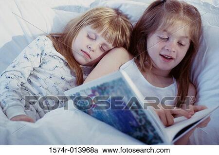 Stock Image - Close-up of two girls reading a book in bed. Fotosearch