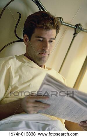 Stock Photo - Close-up of young man reading a newspaper in bed. Fotosearch