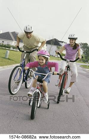 Stock Image - Daughter cycling with her parents. Fotosearch