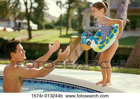 Stock Image - Daughter jumping into her father's arms in a swimming pool. Fotosearch