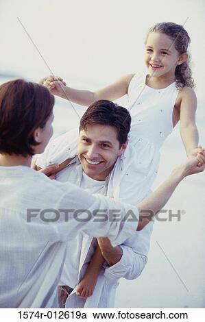 Stock Image - Daughter on her father's shoulders at the beach with her mother standing in front of them. Fotosearch