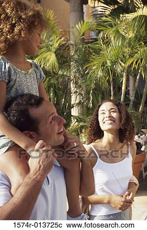 Daughter sitting on her father's shoulders with her mother standing beside them View Large Photo Image Stock Image - Daughter sitting on her father's shoulders with her mother standing beside them. Fotosearch