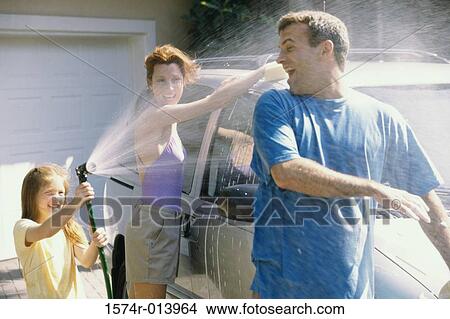Daughter spraying water on her father with her mother washing the car View Large Photo Image Picture - Daughter spraying water on her father with her mother washing the car. Fotosearch